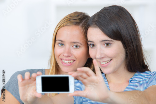 two pretty young funny girls friends smiling and making selfie