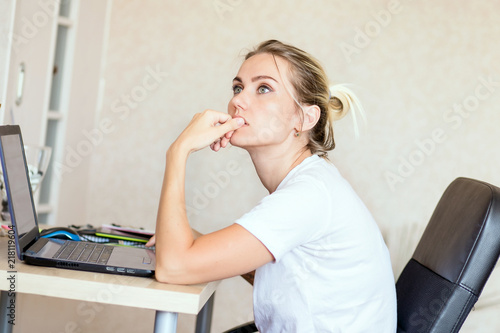 Beautiful blonde woman working on laptop at home. She is thoughtful and focused on work. Freelance, work at home concept.