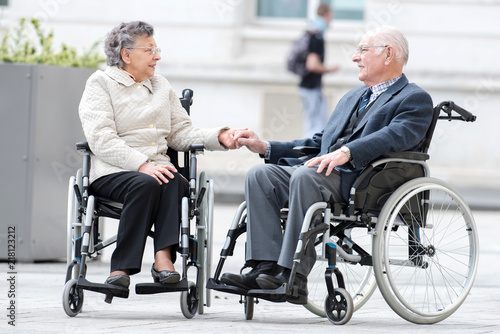 old couple in wheel chair holding hands