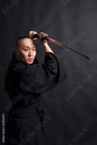 Asian man in black kimano strikes with sword