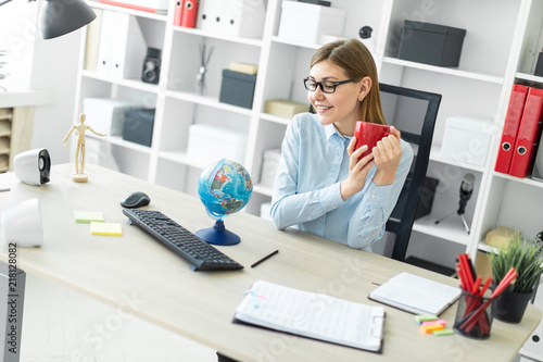 A young girl in glasses is sitting at a table, holding a red cup in her hands and looking at the globe.