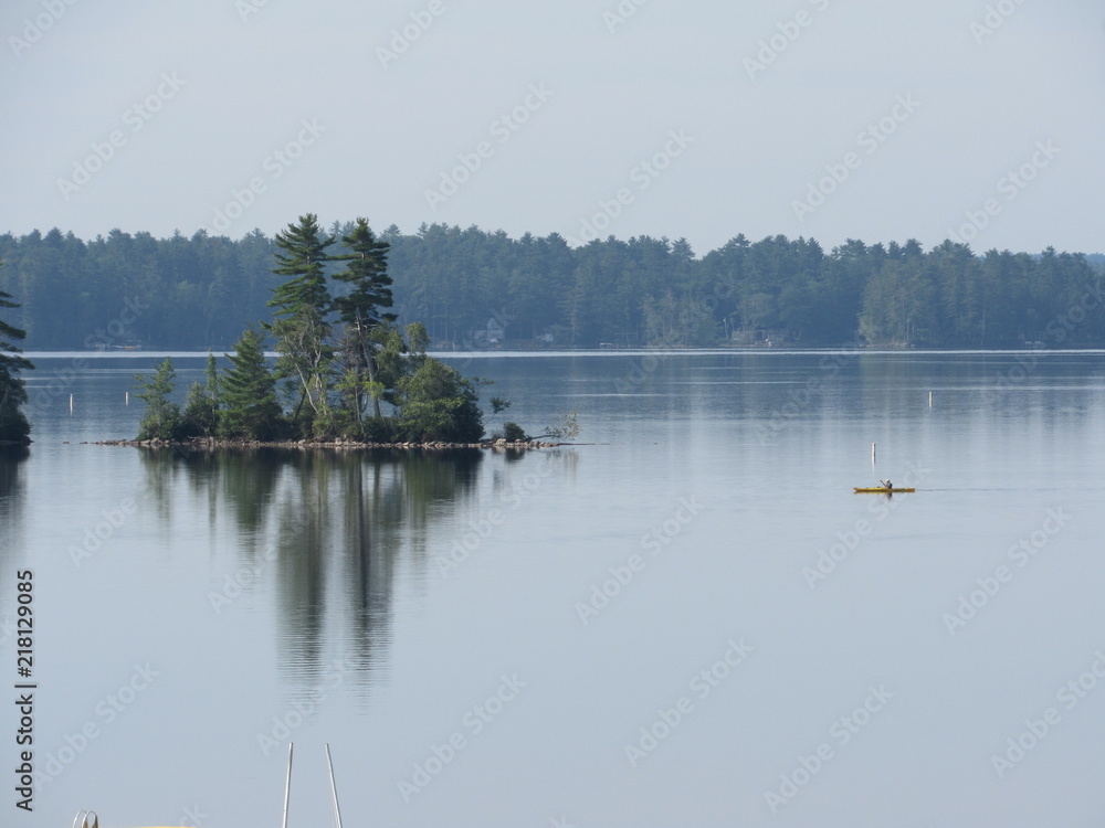 View of Damariscotta Lake in Maine with a person on a kayak passing an island View of Damariscotta Lake in Maine with a person on a kayak passing an island