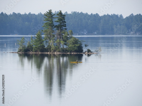View of Damariscotta Lake in Maine with a person on a kayak passing an island  © Isabel
