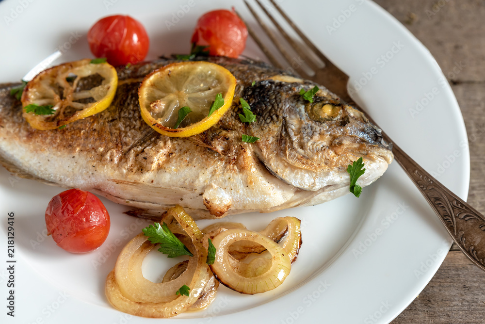 Dorada on plate with onions, lemon and cherry tomatoes Dorada on plate with onions, lemon and cherry tomatoes