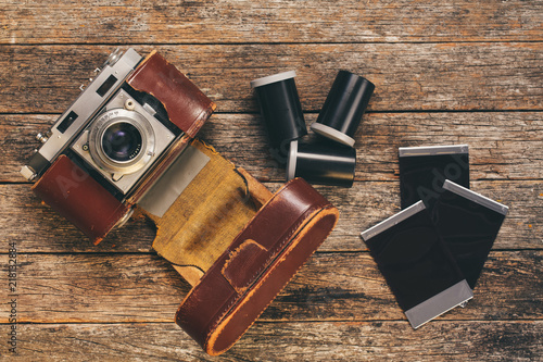 Vintage 35mm film camera in worn leather case with film canisters and prints on weathered wooden background