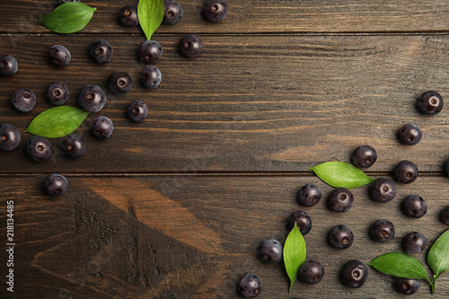 Flat lay composition with fresh acai berries and leaves on wooden background