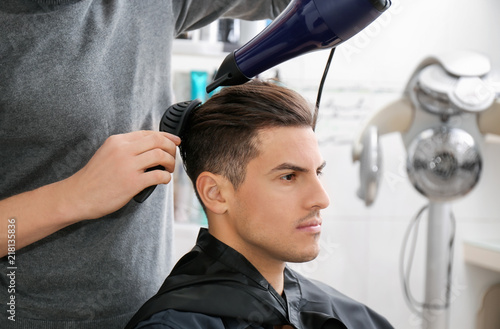 Fotografia Barber making fashionable hairstyle to young man in beauty salon