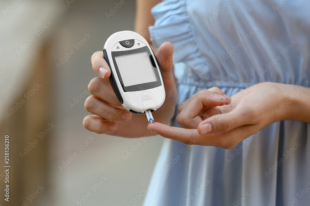 Woman using digital glucometer on blurred background. Diabetes control Woman using digital glucometer on blurred background. Diabetes control