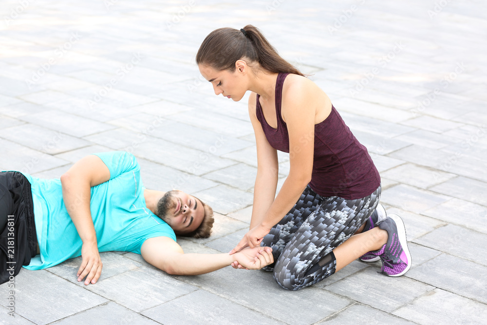 Woman checking pulse of unconscious man outdoors - obrazy, fototapety, plakaty 