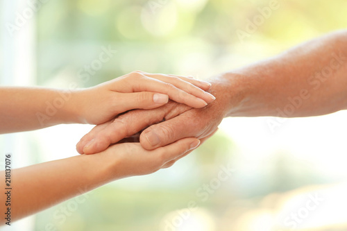 Young woman holding elderly man hand on blurred background, closeup. Help service © New Africa