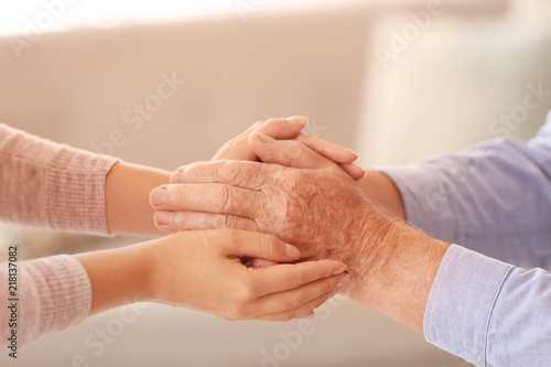 Young woman holding elderly man hands indoors, closeup. Help service