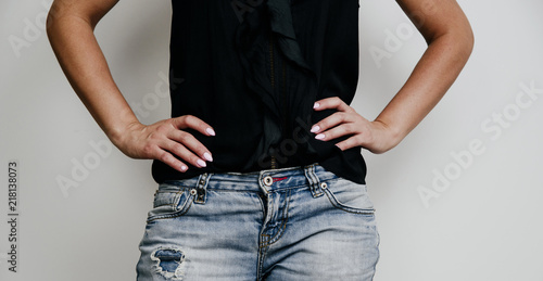 Close-up of a woman's torso. The woman has her hands on her waist. The concept of fashion and fashionable appearance. A girl dressed in blue pants and a black blouse confidently poses.