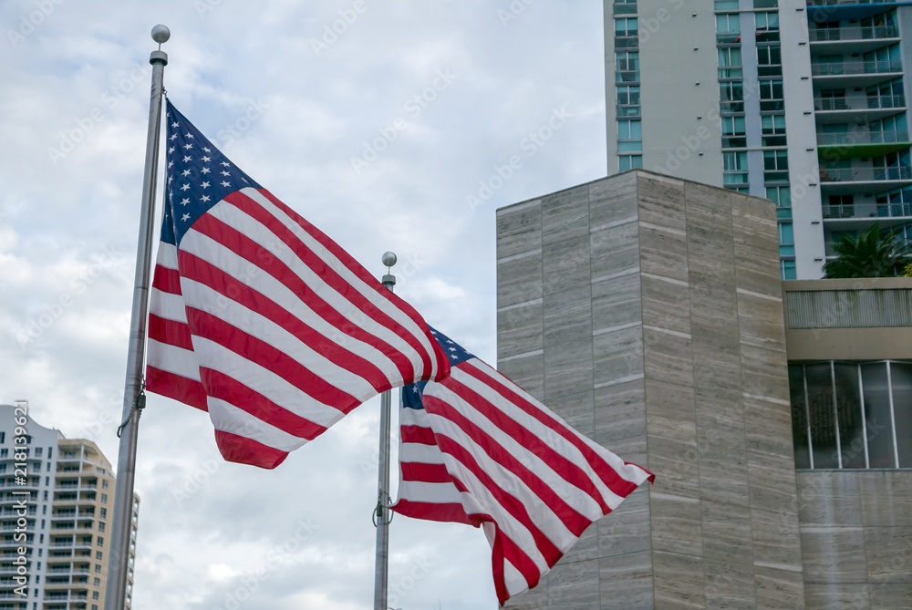 Two american flags waiving on wind on bright cityscape background