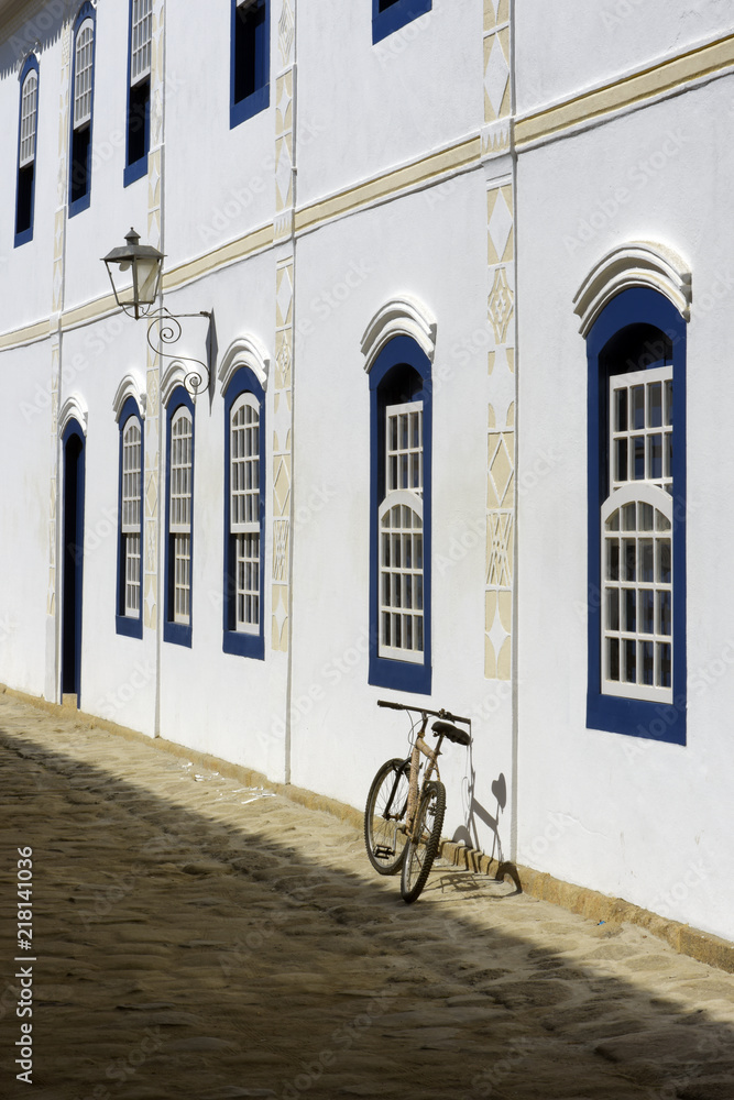 Bicycle parked next to the white wall with blue windows