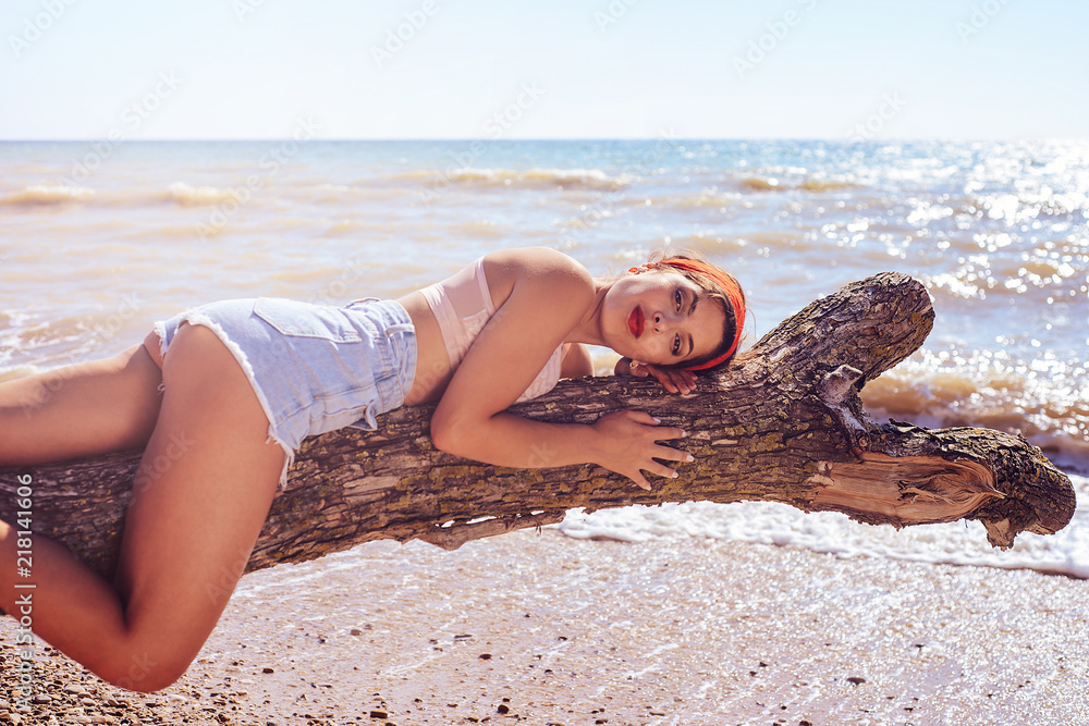 A young sexy girl with a juicy ass lies on an old tree, on the ocean coast  and looks thoughtfully. Stock Photo | Adobe Stock