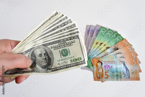 Man hands holding firmly many hundred of US Dollar currency notes against New Zealand currency bills photo