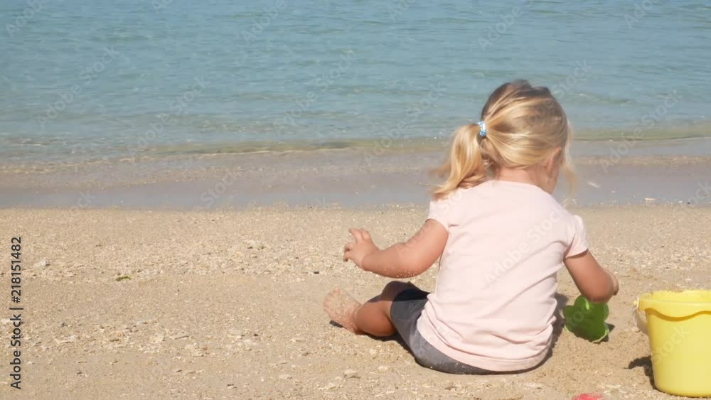 Little Blond Girl Sitting on Beach Playing in Sand by Water Little Blond Girl Sitting on Beach Playing in Sand by Water