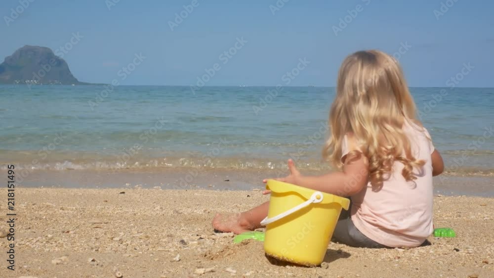 Little Blond Girl Sitting on Beach Playing in Sand with Bucket Little Blond Girl Sitting on Beach Playing in Sand with Bucket