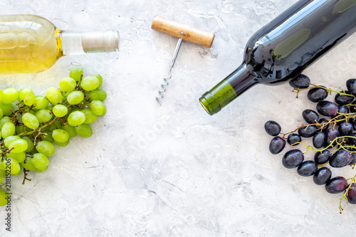 Composition with wine bottles. Red and white wine bottles, bunch of grapes, corkscrew on grey background top view space for text