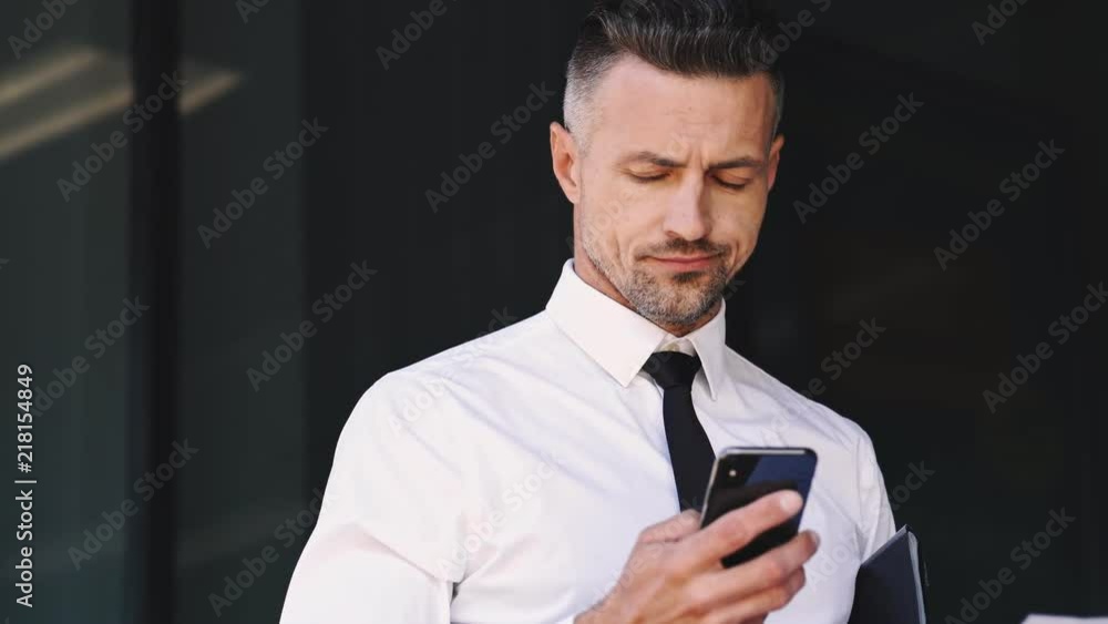 Close up view of serious business man dressed in suit talking by smartphone with documents in hand while standing outside a glass building
Close up view of serious business man dressed in suit talking by smartphone with documents in hand while standing outside a glass building