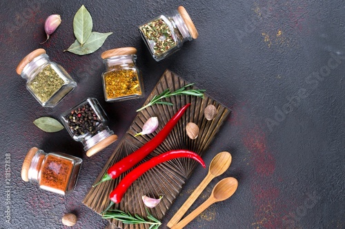 Cooking table with spices in glass jars and herbs. On dark background