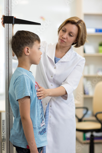 Female doctor measuring height of child boy in clinic