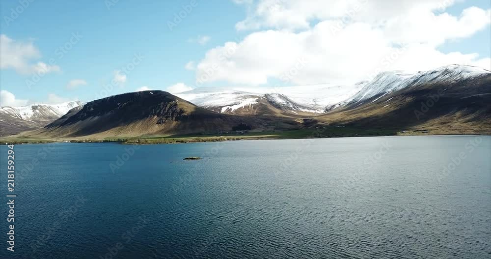 Aerial shot flying over a blue alpine lake with snowy mountains in Haukadalsvatn, Iceland. Aerial shot flying over a blue alpine lake with snowy mountains in Haukadalsvatn, Iceland.
