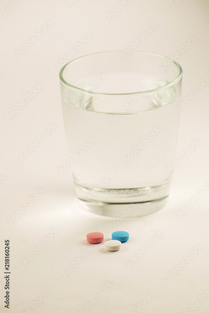 Glass of water and pills on white background. A glass of water and vitamins. Healthy lifestyle, nutritional supplements. Glass of water and pills on white background. A glass of water and vitamins. Healthy lifestyle, nutritional supplements.
