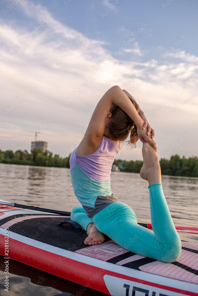 Young beautiful woman meditating in a sea at SUP paddleboarding. Healthy lifestyle.