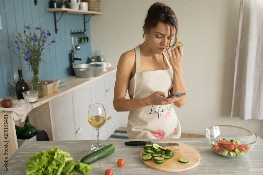 A woman in an apron prepares and uses a smartphone.