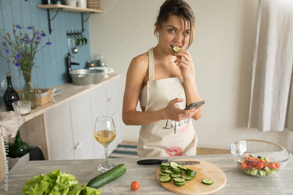 A woman in an apron prepares and uses a smartphone.