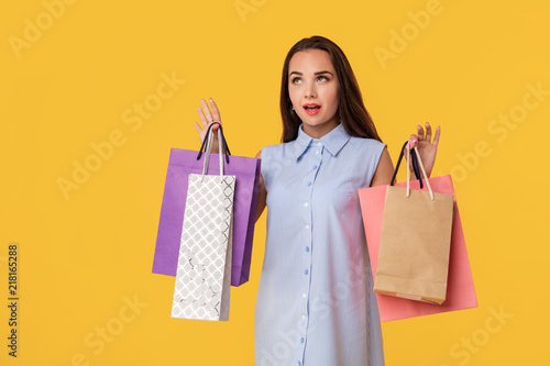 Young brunette lady in white and blue summer striped dress posing with shopping bags over yellow background.