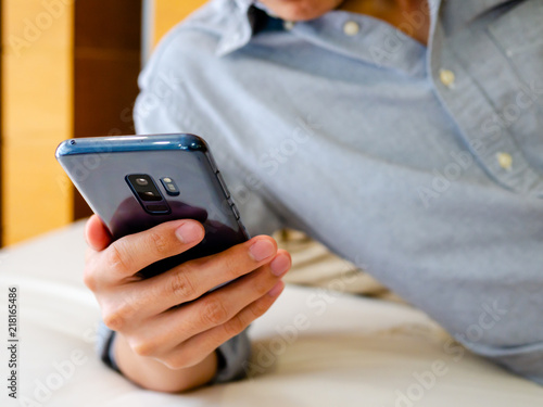 Asian man relaxing with holding and using a smartphone for his working, planning and schedualing or playing games, entertainment, social networking or online payment, smartphone concept, copy space.