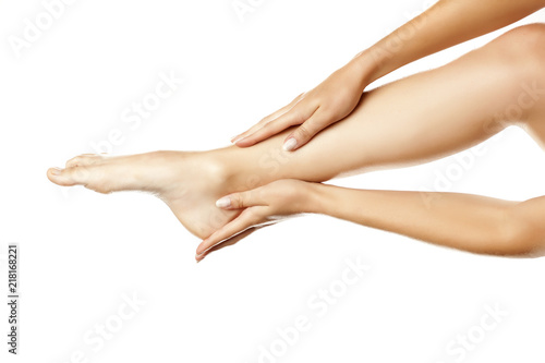 closeup of female hands applying hand cream on leg on white background