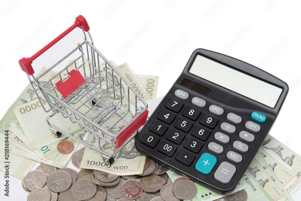 Shopping carts and calculator over stacked coins and banknotes