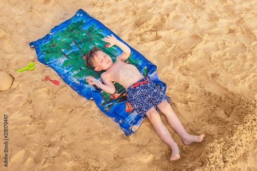 The boy is lying on the beach