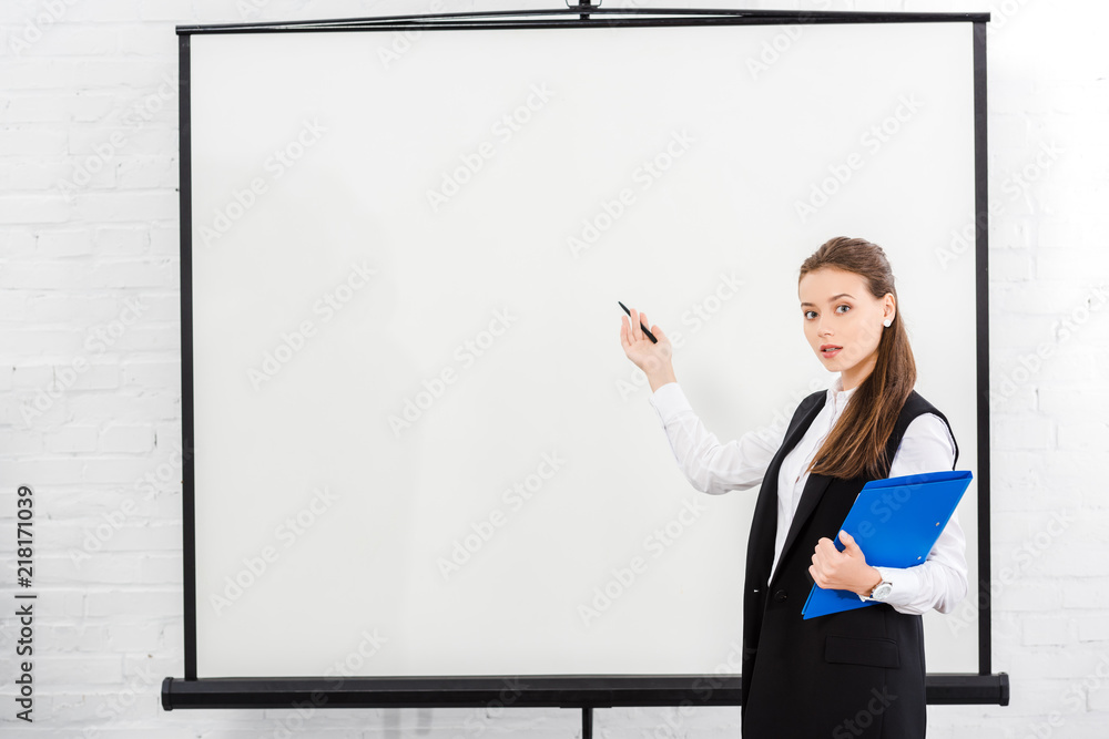 attractive young businesswoman with folder pointing at blank whiteboard at modern office attractive young businesswoman with folder pointing at blank whiteboard at modern office