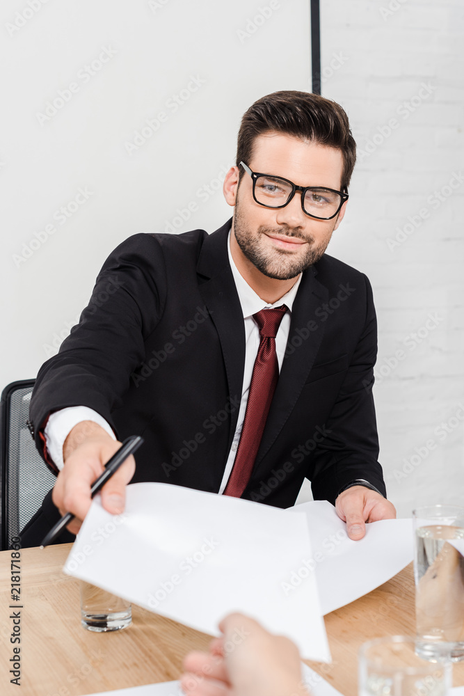 cropped shot of smiling businessman passing blank papers to female colleague at office cropped shot of smiling businessman passing blank papers to female colleague at office