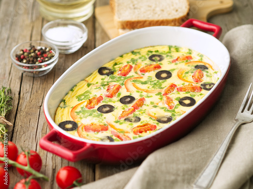 Casserole dish, delicious hot omelette with tomatoes, olives, capsicum. Old wood background, side view