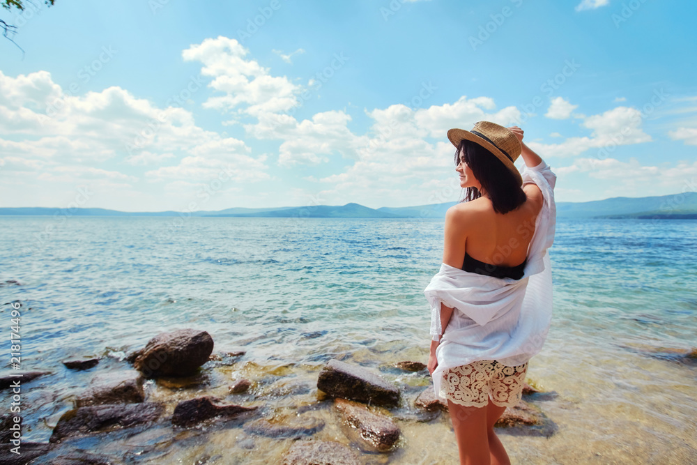A slender woman in a white shirt and hat relaxes near the water