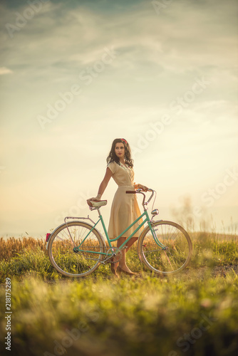 pretty young smilling woman with retro bicycle in sunset on the road, vintage old times, girl in retro style on meadow © martingaal