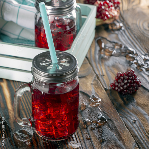 Pomegranate juice with ice in a decanter and a jar on a dark wooden background. Rustic style. photo