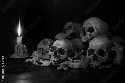 Pile of skulls with bones and Candle which has flame to be bright in the dark light room