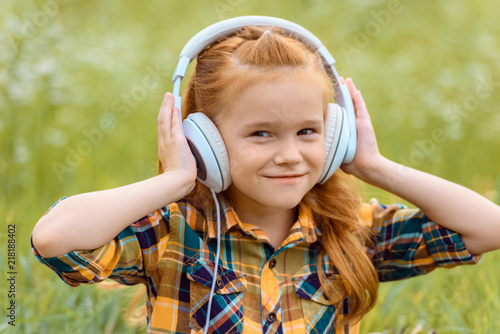 portrait of smiling kid listening music in headphones with green grass on background