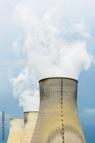 Three natural draft cooling towers of a nuclear power plant releasing clouds of water vapor against a dark stormy sky.