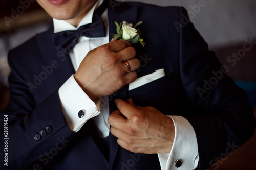 stylish man in black suit and white shirt corrects the boutonier. the groom hands with a boutonier close up portrait  . meeting of the groom. photo