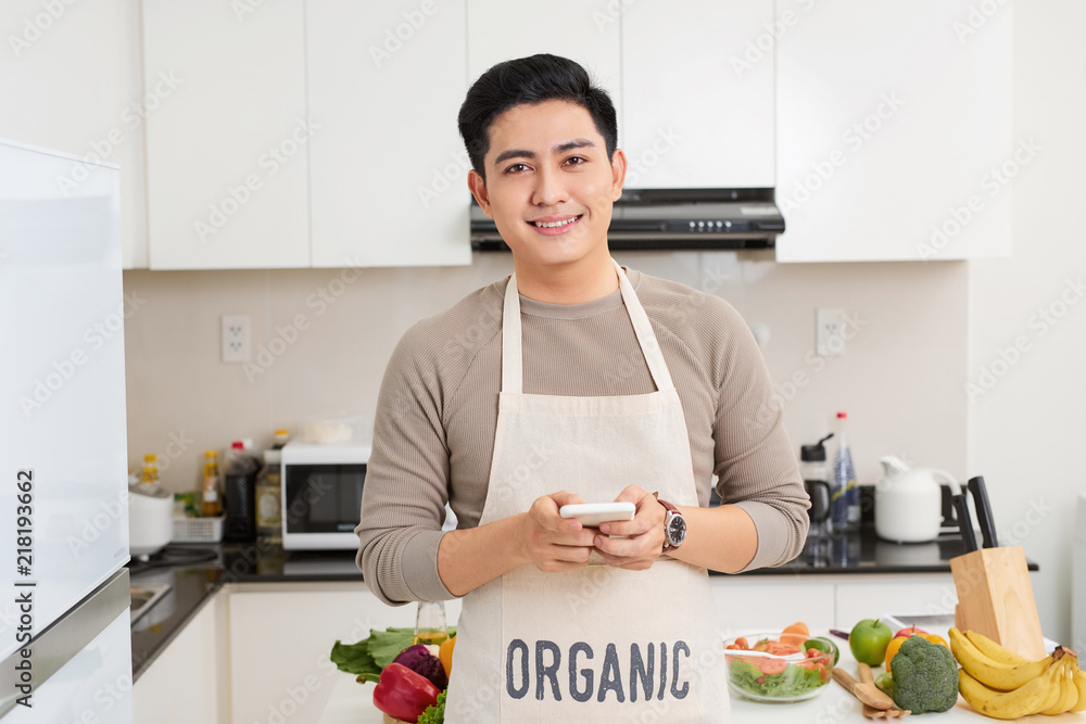 handsome young man using smartphone while cooking