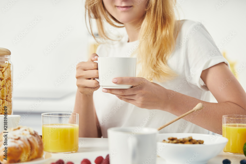 partial view of woman with cup of coffee having breakfast at home partial view of woman with cup of coffee having breakfast at home