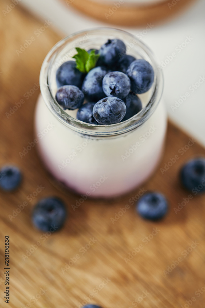 close up view of yogurt with fresh blueberries for breakfast on wooden cutting board close up view of yogurt with fresh blueberries for breakfast on wooden cutting board
