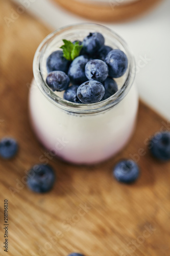 close up view of yogurt with fresh blueberries for breakfast on wooden cutting board